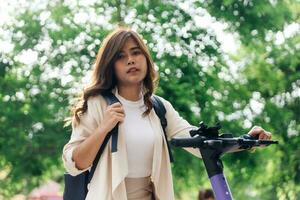 retrato de joven asiático mujer montando eléctrico scooter en parque foto