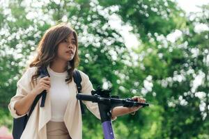 joven asiático mujer en casual vestir montando eléctrico scooter en parque foto