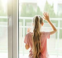 Sad little girl looking through  window at home. photo