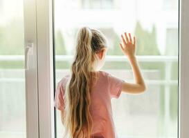 Sad little girl looking through  window at home. photo