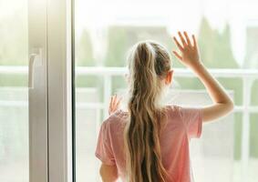 Sad little girl looking through  window at home. photo