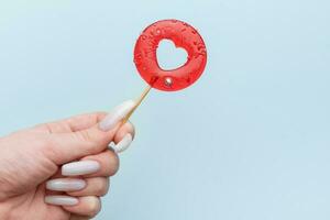 Woman female hand holding heart shaped lollipop on blue background. photo