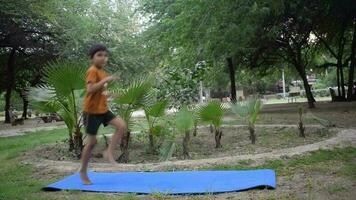 Aziatisch slim kind aan het doen yoga houding in de maatschappij park buitenshuis, kinderen yoga houding. de weinig jongen aan het doen yoga en meditatie oefening. video