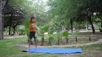 Aziatisch slim kind aan het doen yoga houding in de maatschappij park buitenshuis, kinderen yoga houding. de weinig jongen aan het doen yoga en meditatie oefening. video