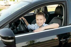 A cute boy is sitting behind the wheel of a car and smiling photo