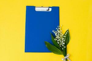 A blue folder as a template with a place to copy on a yellow table with lilies of the valley photo