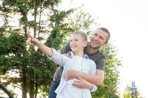 Dad hugs a happy boy standing near the car in the woods the bright sun. The concept of a family day. photo