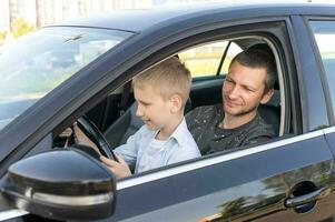 Dad and son in the front seat of the car at the wheel. The boy holds the steering wheel photo
