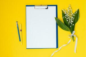 A blue folder a template with a place to copy on a yellow table with lilies of the valley and pens photo