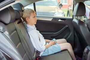 Cute sad boy sitting in a car wearing a seat belt photo