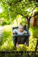 linda pequeño niña en el balancearse. bebé columpio en el árbol en el jardín. infantil jugando en el patio interior foto