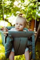 linda pequeño niña en el balancearse. bebé columpio en el árbol en el jardín. infantil jugando en el patio interior foto