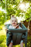 linda pequeño niña en el balancearse. bebé columpio en el árbol en el jardín. infantil jugando en el patio interior foto