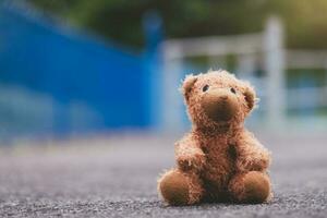 Lost teddy bear toy sitting  on playground floor in gloomy day,Lonely and sad brown bear doll sitting alone in the park, Lost toy or Loneliness concept,International missing Children day photo