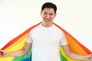 Cheerful young man wrapped in rainbow flag enjoying isolated on white background. Homosexual lgbtiq concept, rainbow flag, celebrating parade. Copy space. photo