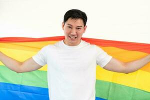 Cheerful young man wrapped in rainbow flag enjoying isolated on white background. Homosexual lgbtiq concept, rainbow flag, celebrating parade. Copy space. photo