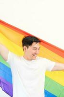 Cheerful young man wrapped in rainbow flag enjoying isolated on white background. Homosexual lgbtiq concept, rainbow flag, celebrating parade. Copy space. photo