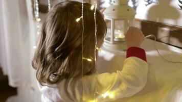 peu garçon dans Noël pyjamas décorer le fenêtre avec Noël ornements et Noël lumière video