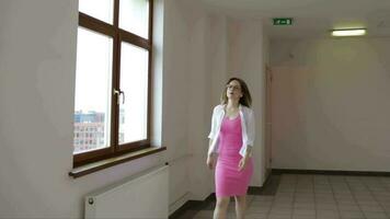 Young woman in a bright pink dress and white cardigan walking on a corridor video