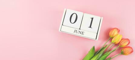 flat lay of wooden calendar June 01 with tulips flower bouquet on pink background with copy space, wide banner. photo