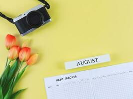 flat lay of habit tracker book, digital camera and red yellow tulips flowers on yellow background with copy space. photo