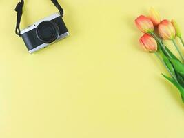 flat lay of digital camera and tulips flowers with copy space on yellow background. photo