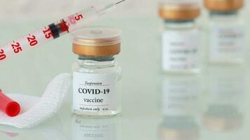 Glass vial of COVID-19 vaccine and syringe on a glass surface. Closeup video