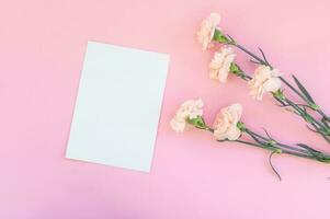 Top view of a pink table with a layout of empty notebooks and a bouquet of carnations. Place for text photo