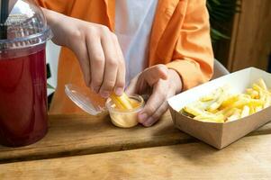 el niño manos sostener francés papas fritas y inmersión ellos en queso salsa. rojo limonada foto