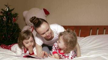 Young mother between 30 and 35 years old reads fairy tales to her small children in the bed. Winter holidays period. video