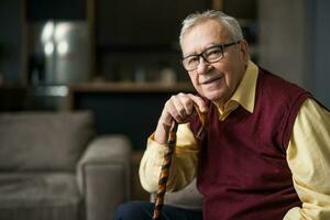 Happy senior man is sitting on bed in his home. Portrait of senior man with walking cane. photo