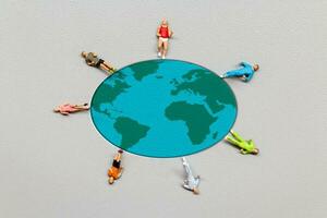 Miniature people standing on the globe with gray background photo