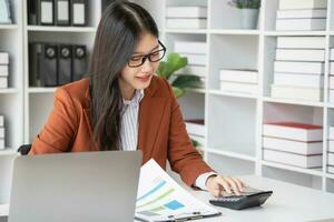 mujer de negocios trabajando en el oficina utilizando calculadora a calcular financiero informes. ventas datos con ordenador portátil computadora y negocio documentos en oficina mesa. cerca arriba. negocio Finanzas y inversión. foto