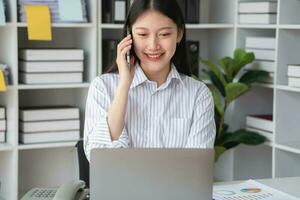 asiático mujer de negocios hablando en el teléfono trabajando en moderno oficina charla con clientela para un nuevo camino de haciendo negocio en el oficina. foto