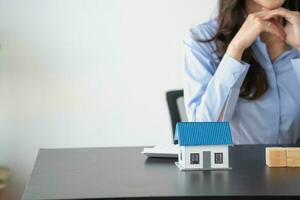 Asian woman with long hair in blue shirt enjoying saving money for house purchase through piggy bank savings concept. photo