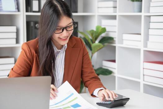 businesswoman working in the office Using calculator to calculate financial reports. Sales data with laptop computer and business documents on office table. Close up. Business finance and investment. photo
