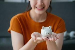 Young Asian woman saving for retirement Saving money through a piggy bank and taking notes on notebook, savings concept. photo