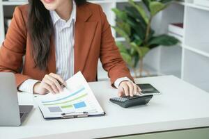 mujer de negocios trabajando en el oficina utilizando calculadora a calcular financiero informes. ventas datos con ordenador portátil computadora y negocio documentos en oficina mesa. cerca arriba. negocio Finanzas y inversión. foto