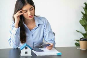 Asian woman with long hair in the blue shirt is using a credit card for buying a new house and looking at home-buying documents The idea of purchasing a home with a credit card. photo