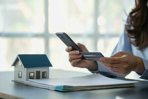 Asian woman with long hair in the blue shirt is using a credit card for buying a new house and looking at home-buying documents The idea of purchasing a home with a credit card. photo