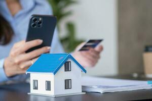 Asian woman with long hair in the blue shirt is using a credit card for buying a new house and looking at home-buying documents The idea of purchasing a home with a credit card. photo