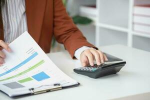 businesswoman working in the office Using calculator to calculate financial reports. Sales data with laptop computer and business documents on office table. Close up. Business finance and investment. photo