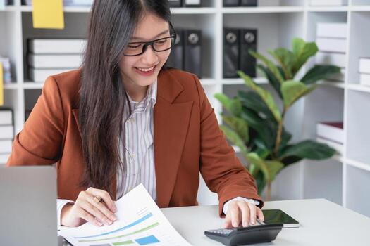 businesswoman working in the office Using calculator to calculate financial reports. Sales data with laptop computer and business documents on office table. Close up. Business finance and investment. photo