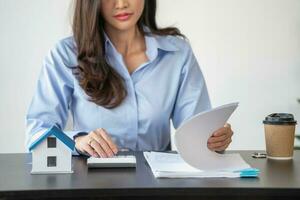 asiático mujer con largo pelo en el azul camisa es utilizando un crédito tarjeta para comprando un nuevo casa y mirando a comprar casa documentos el idea de adquisitivo un hogar con un crédito tarjeta. foto