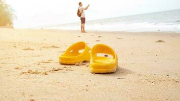 Tourists take off their yellow flip-flops at the beach to walk on the sand barefoot and take pictures, eco-tourism photo