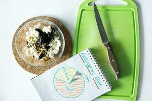 Cooking Breakfast on a Keto diet. cottage cheese with walnuts and prunes. Folding ingredients into a single bowl. Diet with nutrition diagram written on a note. Cooking process, step 4. photo