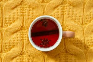 Karkade tea in an orange cup on an orange knitted background. The concept of the autumn season, natural colors. Red fruit tea. photo