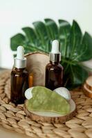 Jade Gua sha scraper and bottles of cosmetic serum for the face on wooden stands. photo