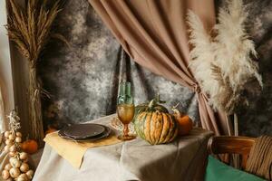 Autumn interior. A table covered with dishes, pumpkins, chair, casual arrangement of Japanese pampas grass. Interior in the photo Studio.