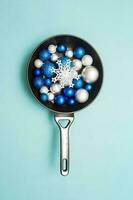 Blue and silver Christmas balls in a frying pan on a turquoise background. Creative concept of Christmas and New year. photo